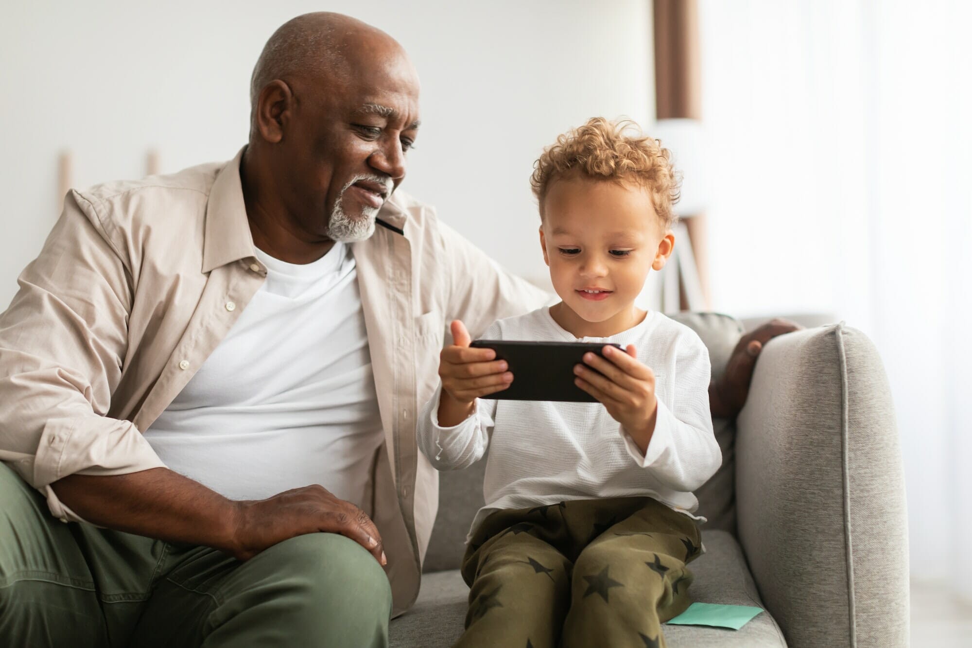 African Grandfather And Grandson Using Smartphone Playing Games At Home, Mobile Game Development for IOS