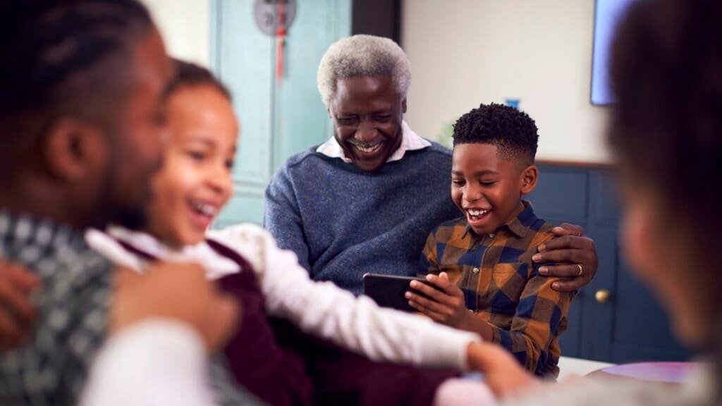 Grandfather With Grandchildren Playing Game On Mobile Phone At Home