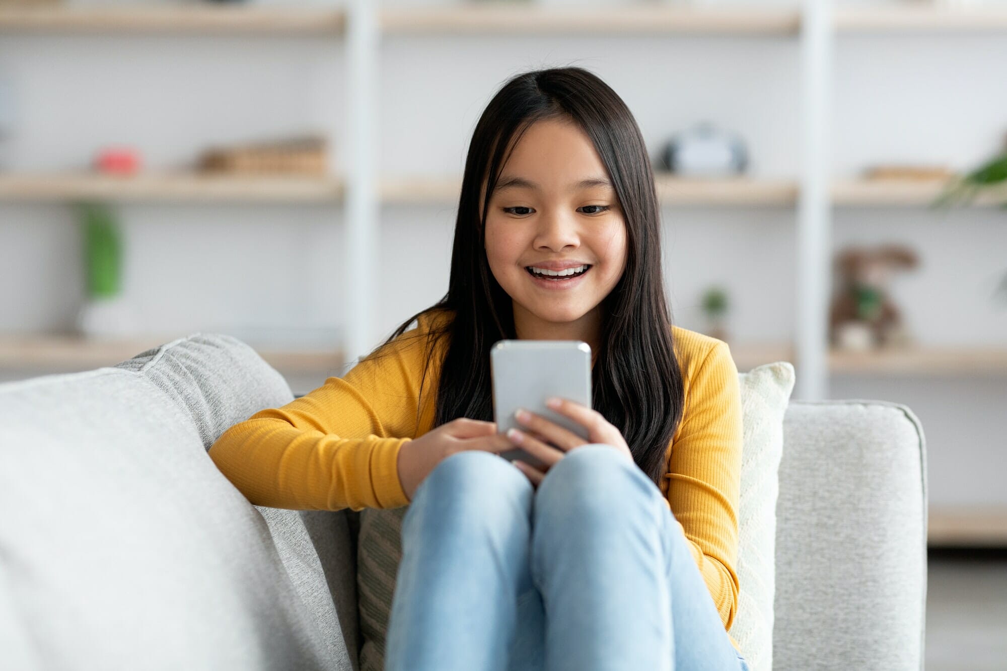 Happy asian girl schooler playing games on cellphone