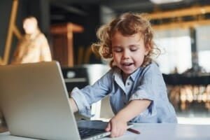 Smart child in casual clothes using laptop for education purposes or fun