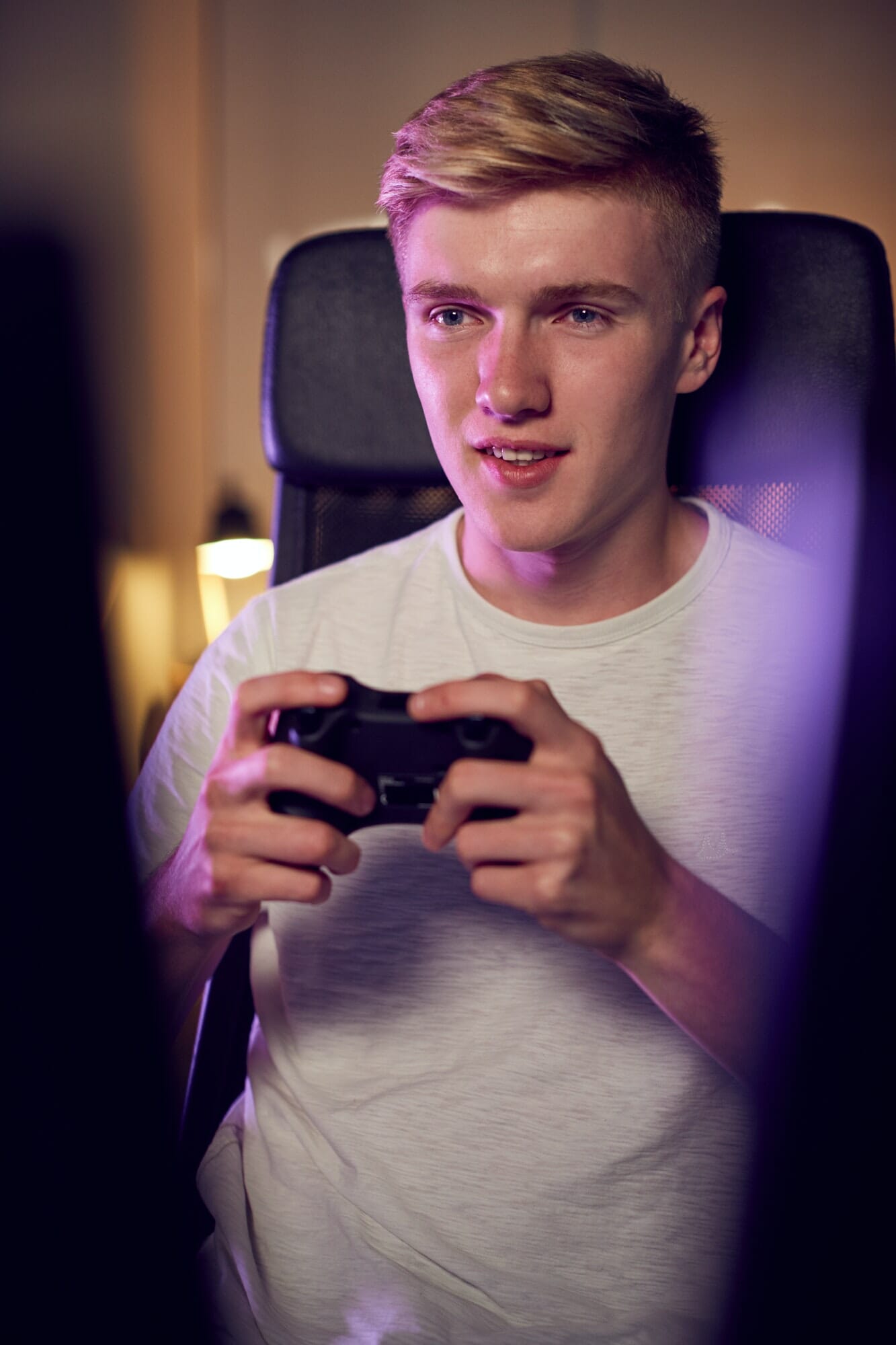 Teenage Boy With Game Pad Sitting In Chair and Gaming At Home