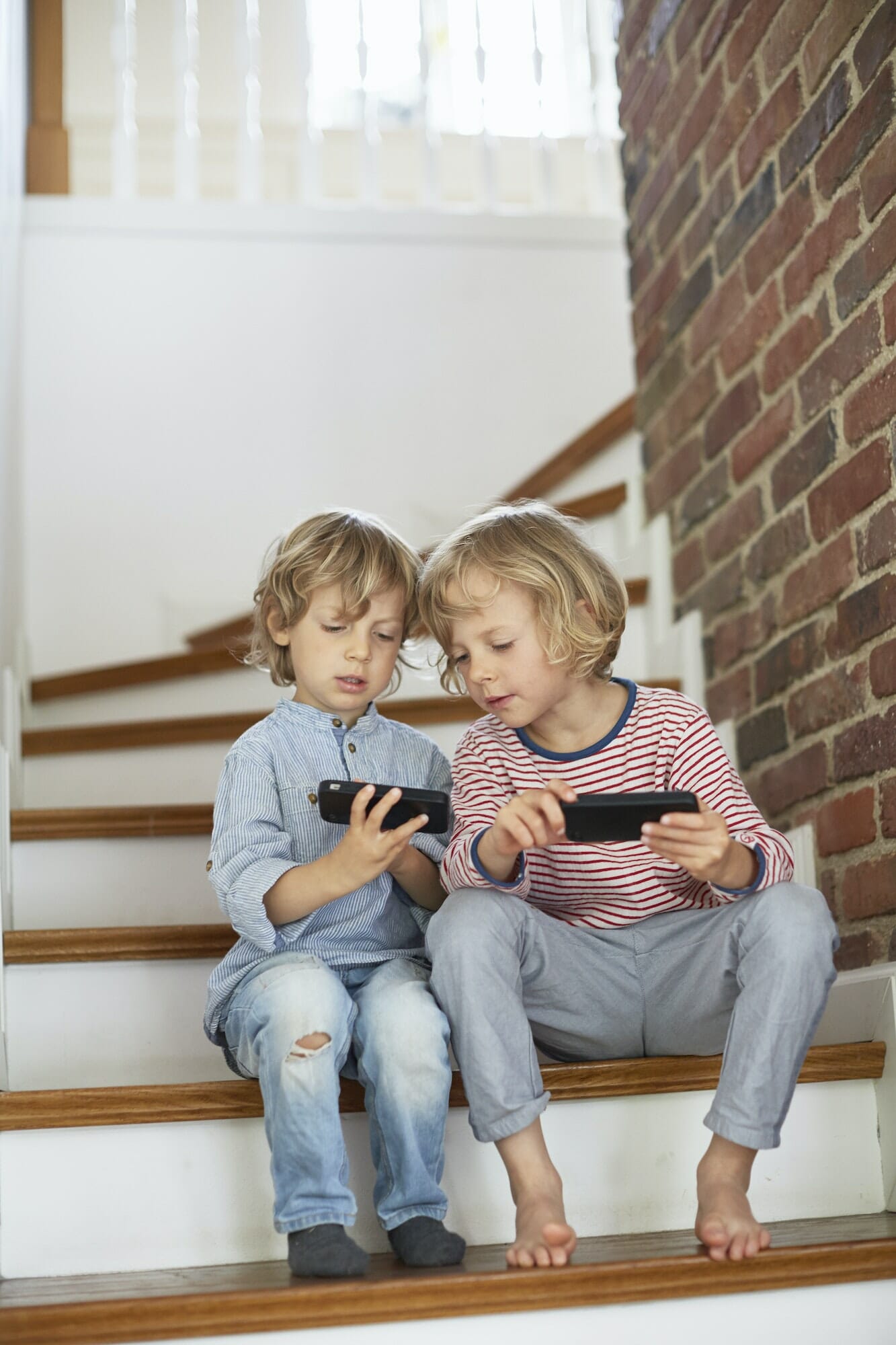 Two young boys, sitting on stairs, looking at smartphones