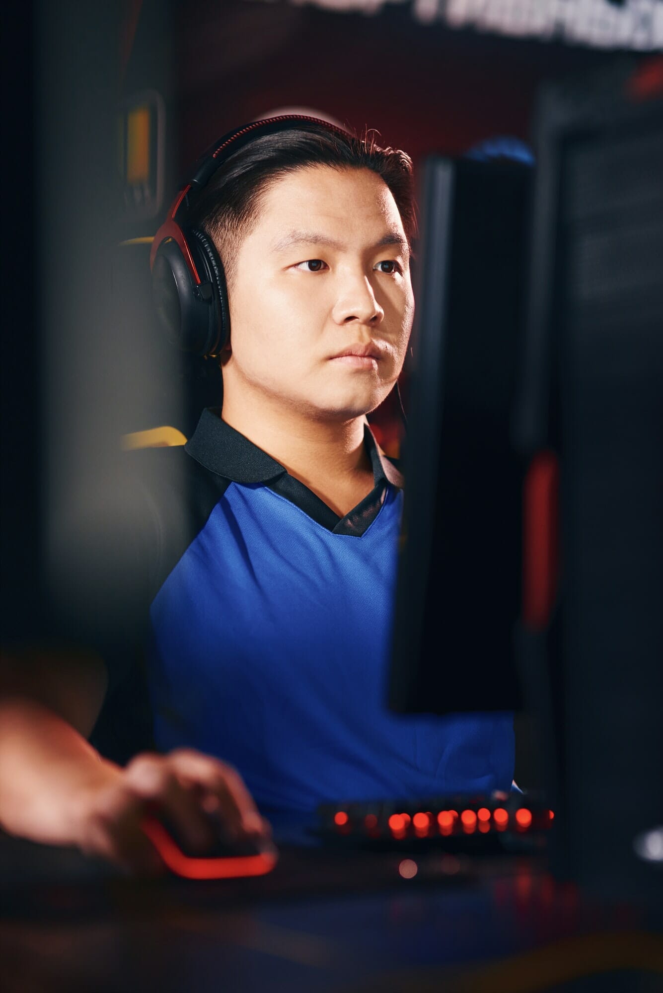 Vertical shot of concentrated asian guy, male cyber sport gamer wearing headphones looking at PC