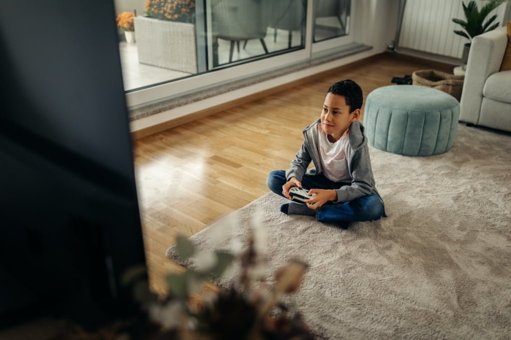 Little afro boy playing video game while sitting on the floor in the living room