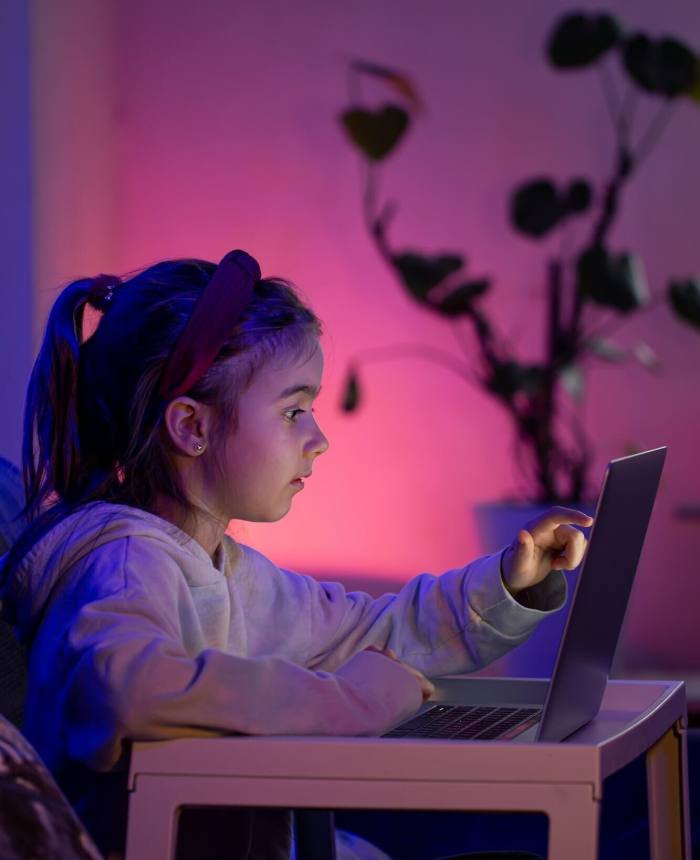 A little girl using a laptop late at night.