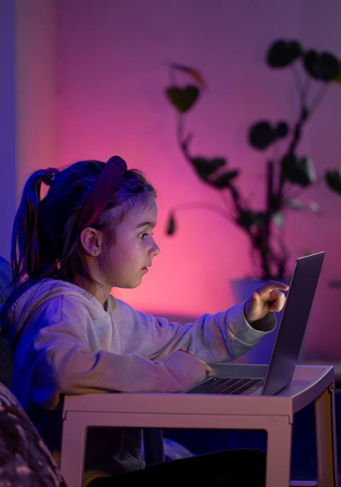 A little girl using a laptop late at night.