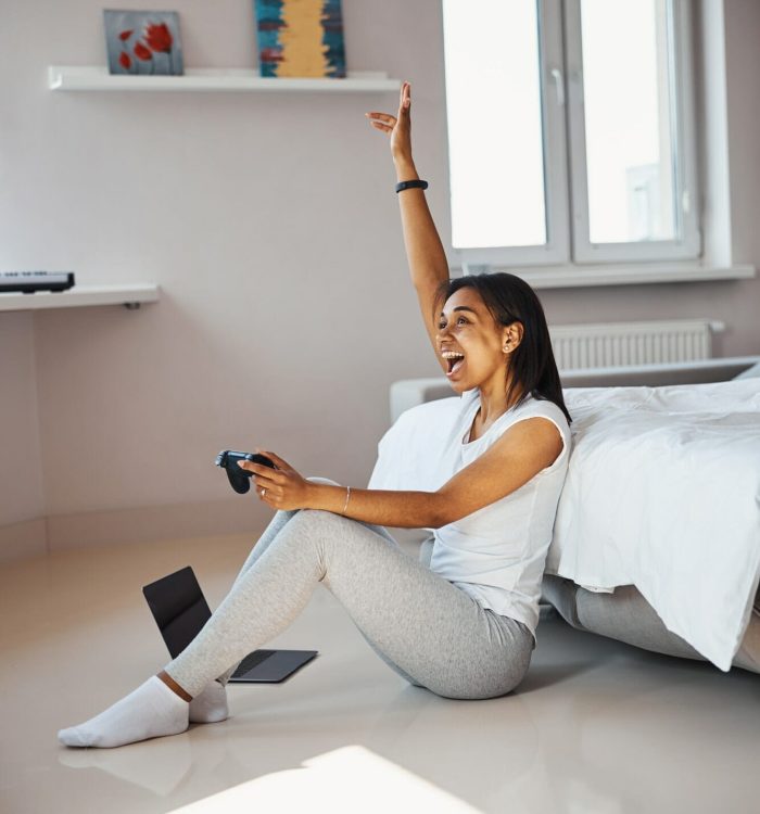 Mobile Game Development for iOS Devices Woman celebrating after winning a game while holding a controller in a modern room.
