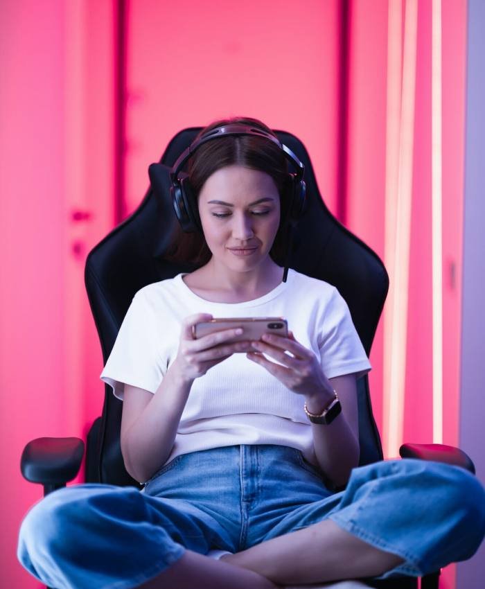 Cybersport gamer playing mobile game on the smart phone sitting on a gaming chair in neon color room