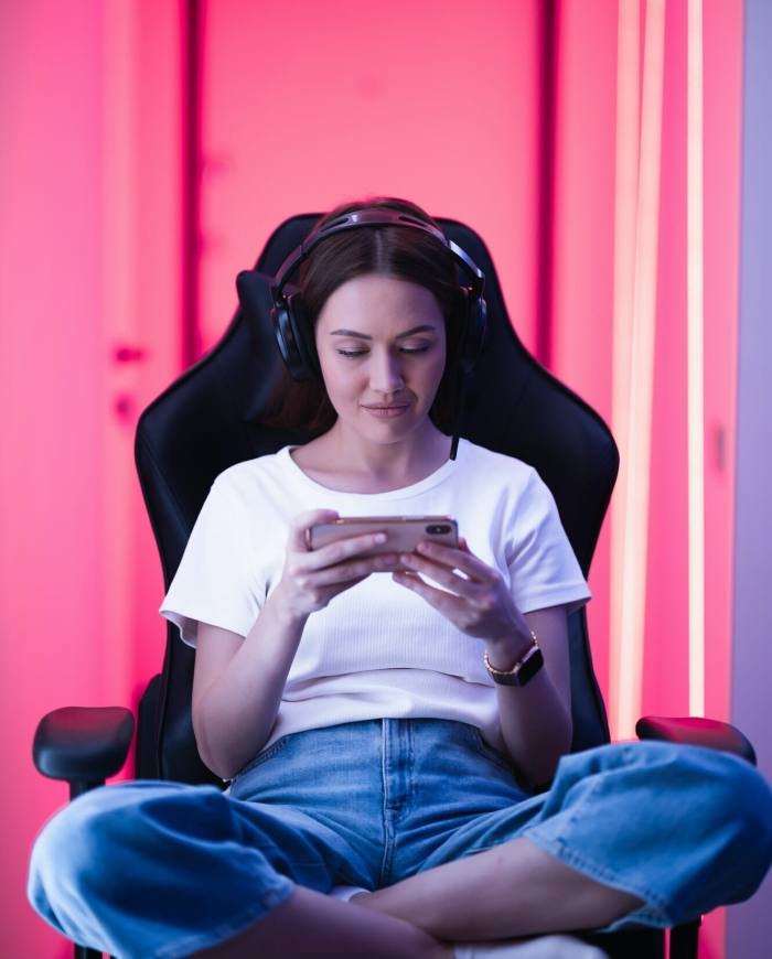 Cybersport gamer playing mobile game on the smart phone sitting on a gaming chair in neon color room