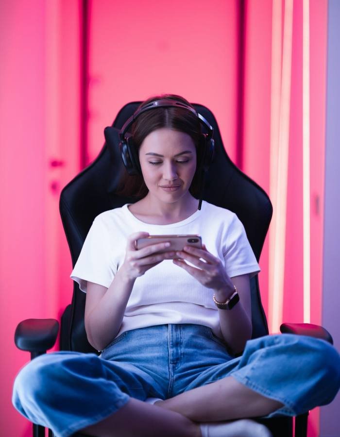 Cybersport gamer playing mobile game on the smart phone sitting on a gaming chair in neon color room