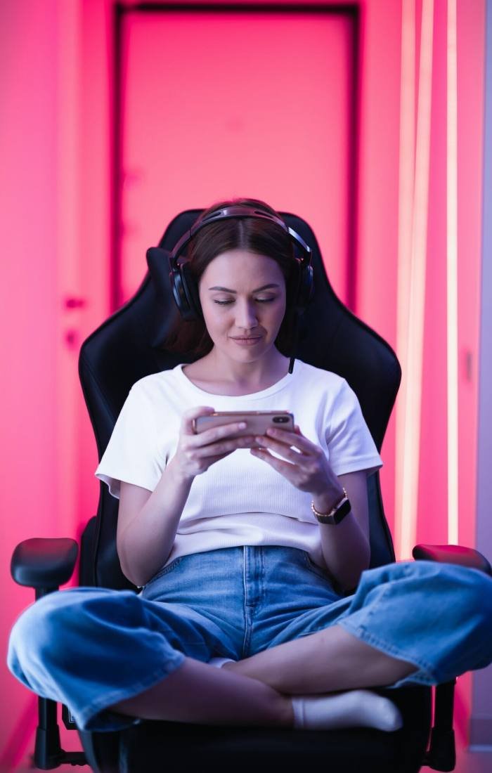 Cybersport gamer playing mobile game on the smart phone sitting on a gaming chair in neon color room