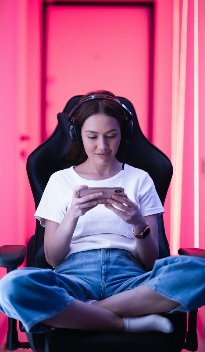 Cybersport gamer playing mobile game on the smart phone sitting on a gaming chair in neon color room