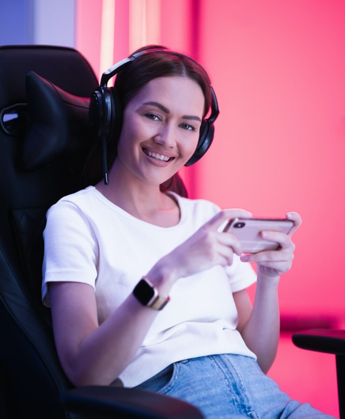 Cybersport gamer playing mobile game on the smart phone sitting on a gaming chair in neon color room