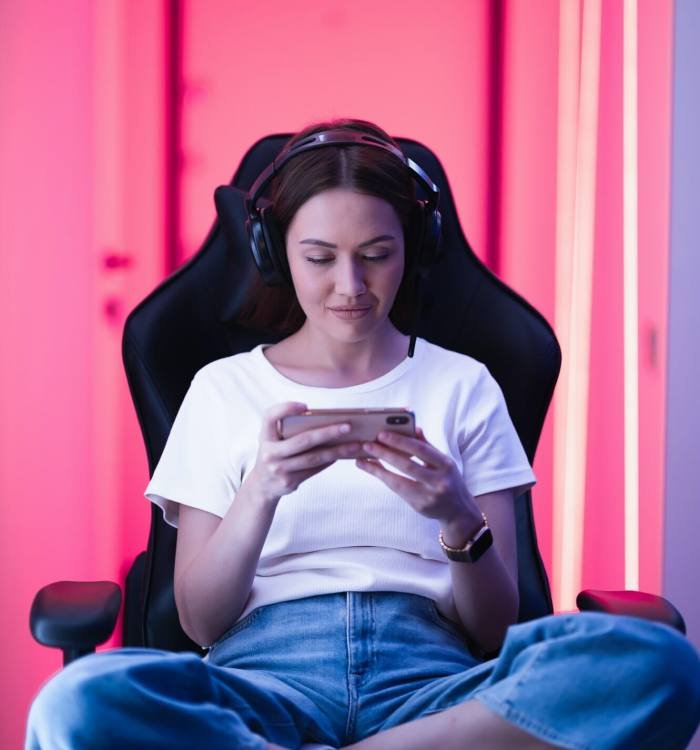 Cybersport gamer playing mobile game on the smart phone sitting on a gaming chair in neon color room, Game Development for Content Creators