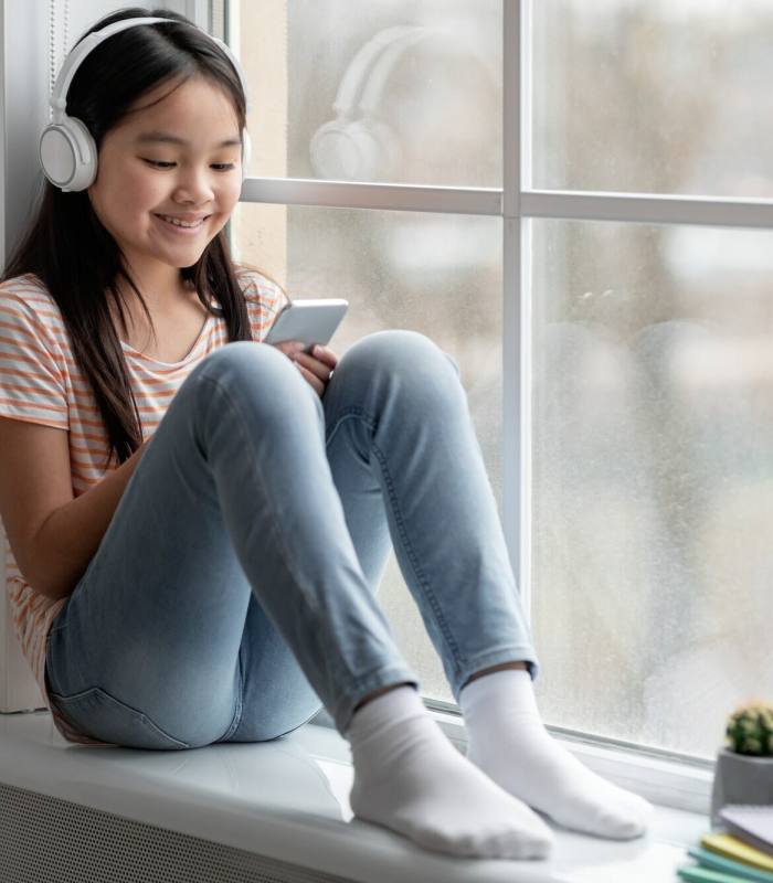 Happy chinese child using headset and smartphone at home