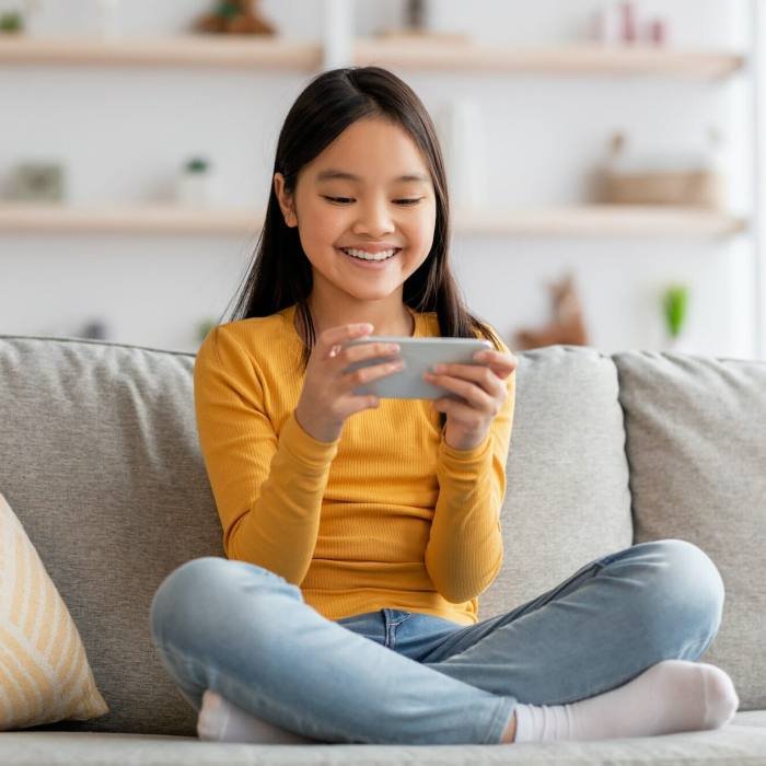 Joyful korean girl schooler playing games on cellphone