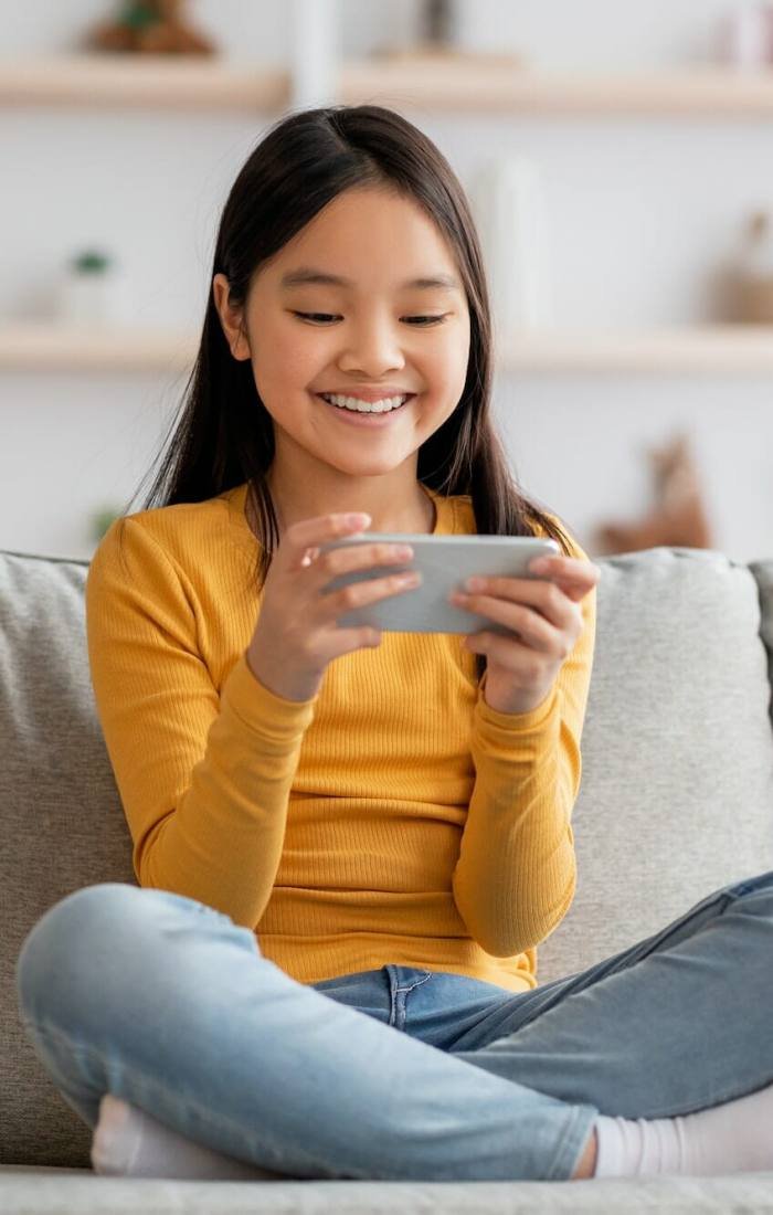 Joyful korean girl schooler playing games on cellphone