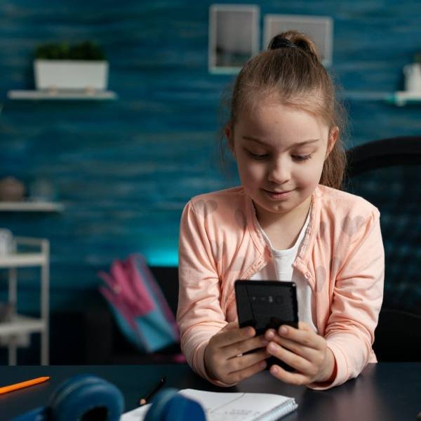 Little schoolchild holding modern smartphone