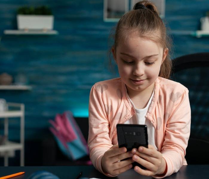 Little schoolchild holding modern smartphone