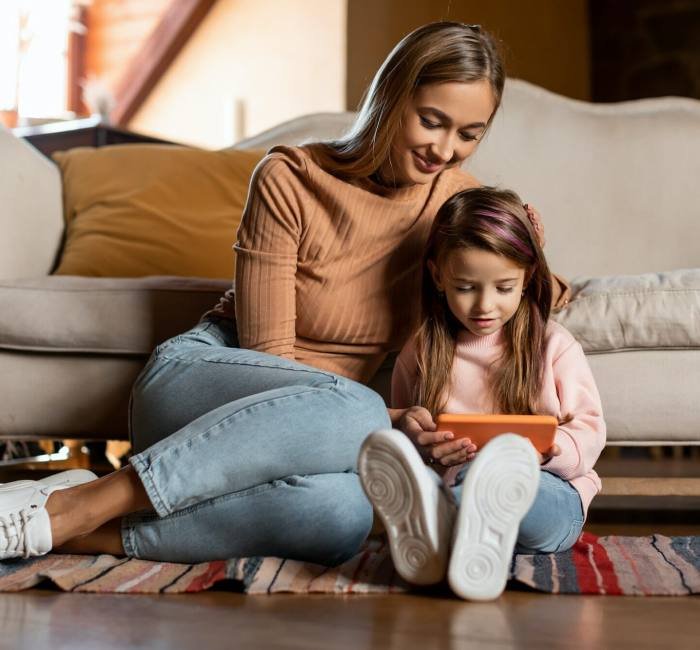 Portrait of smiling mom and daughter using smartphone at home