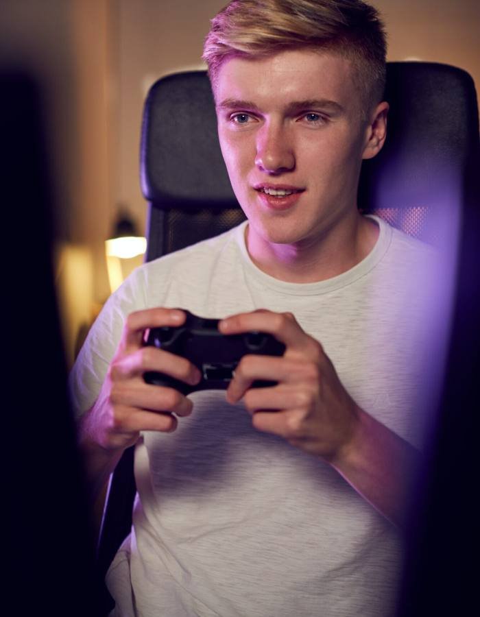 Teenage Boy With Game Pad Sitting In Chair and Gaming At Home