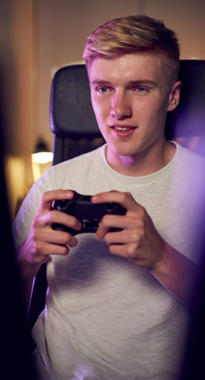 Teenage Boy With Game Pad Sitting In Chair and Gaming At Home