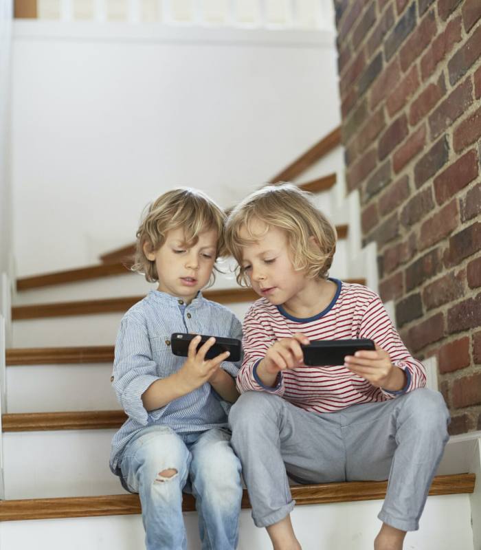 Two young boys, sitting on stairs, looking at smartphones