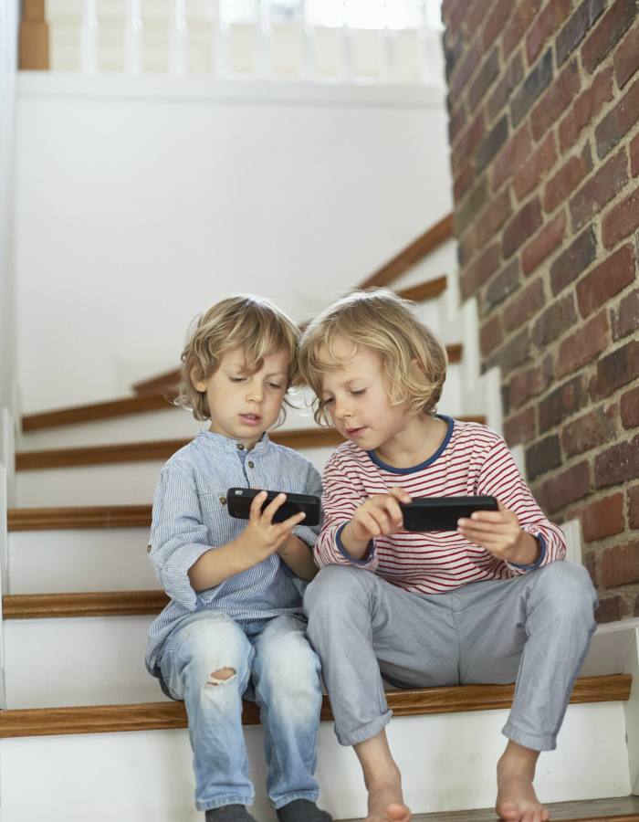 Two young boys, sitting on stairs, looking at smartphones