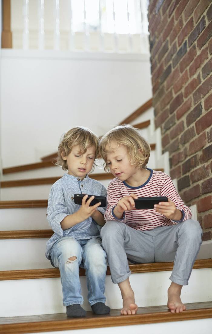 Two young boys, sitting on stairs, looking at smartphones