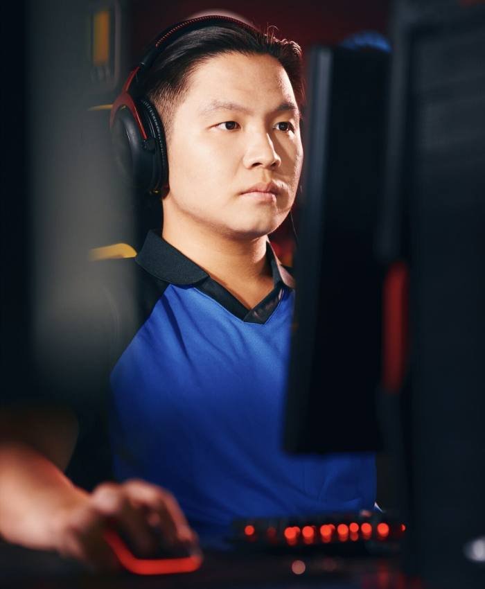 Vertical shot of concentrated asian guy, male cyber sport gamer wearing headphones looking at PC