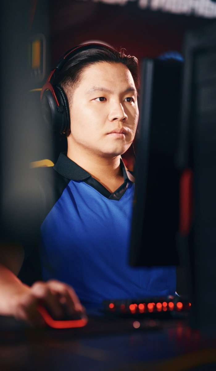 Vertical shot of concentrated asian guy, male cyber sport gamer wearing headphones looking at PC
