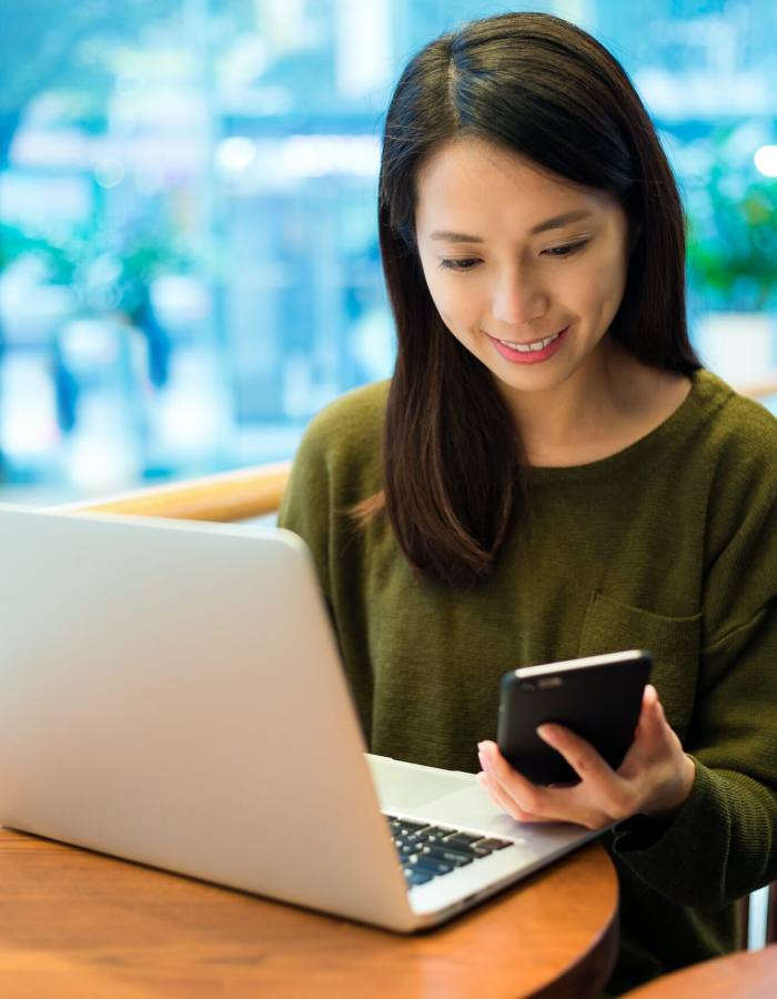 Woman working on laptop computer with cellphone