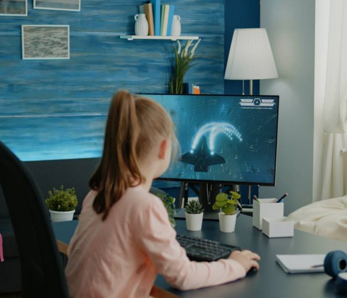 Young girl playing shoot video games on computer at desk