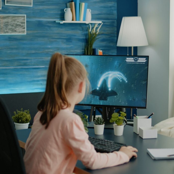 Young girl playing shoot video games on computer at desk