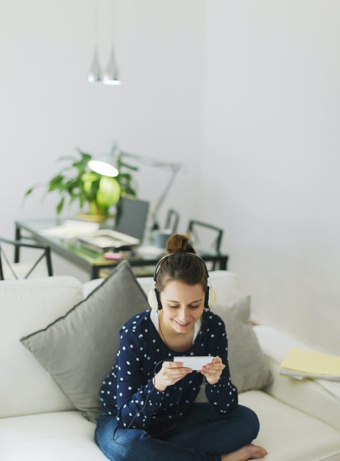 Mobile Game Development for iOS Devices Woman playing a mobile game on her smartphone while sitting comfortably on a sofa.